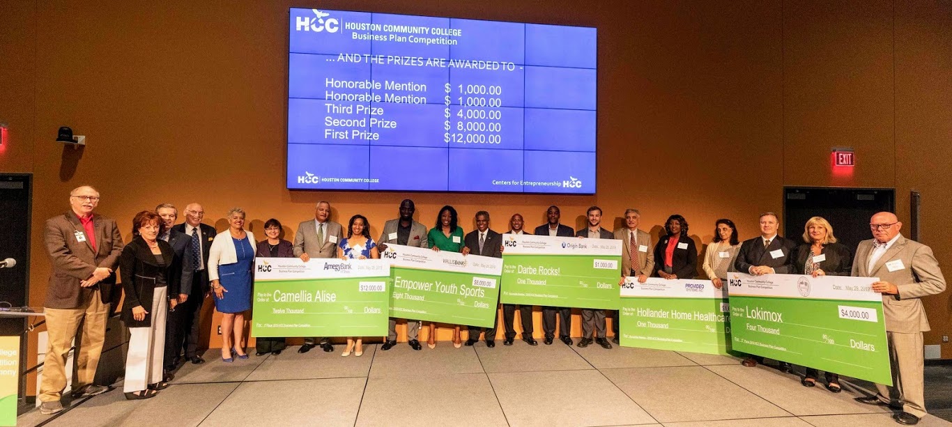 2019 Business Plan Competition Winners take a picture onstage with their teams, showcasing big, green checks with their winnings.